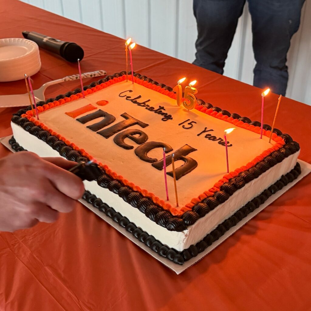 intech's 15 year celebration cake on a table with someone about to cut it